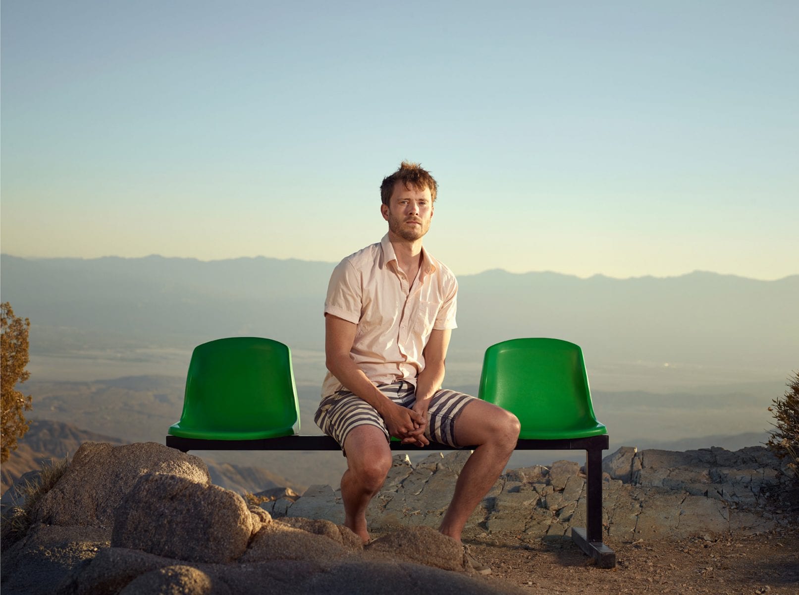 man sitting on a green bench, color portrait photography by dylan collard