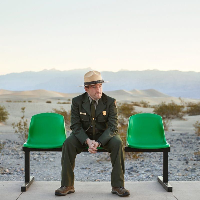 man wearing a hat and sitting on a green bench, color portrait photography by dylan collard