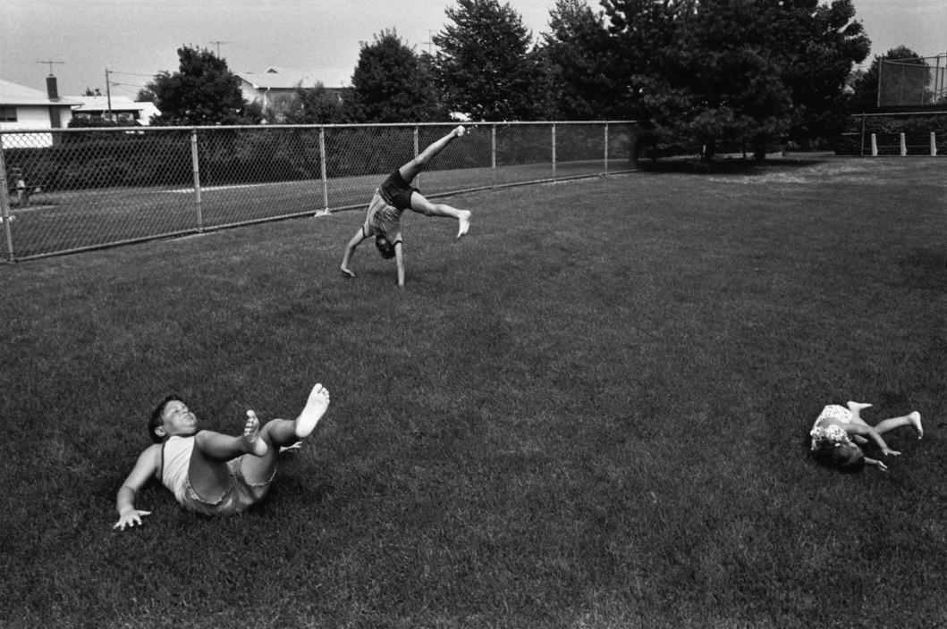 Black and white street photography by Richard Kalvar of kids playing in the grass. Shot in New York, Long Island