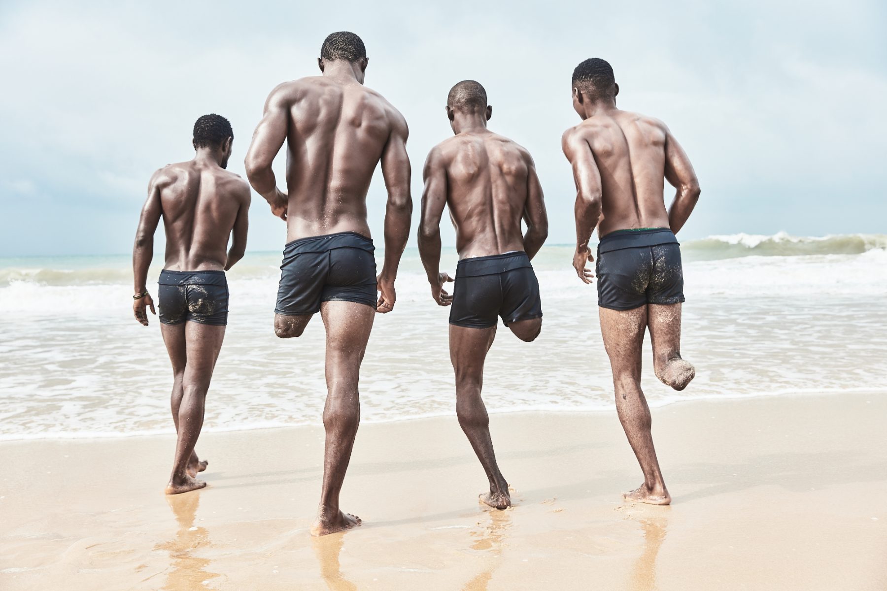 Group portrait by Jack Lawson. “The Special Eagles”, Nigeria’s amputee football team walk towards the sea on the beach outside Lagos.