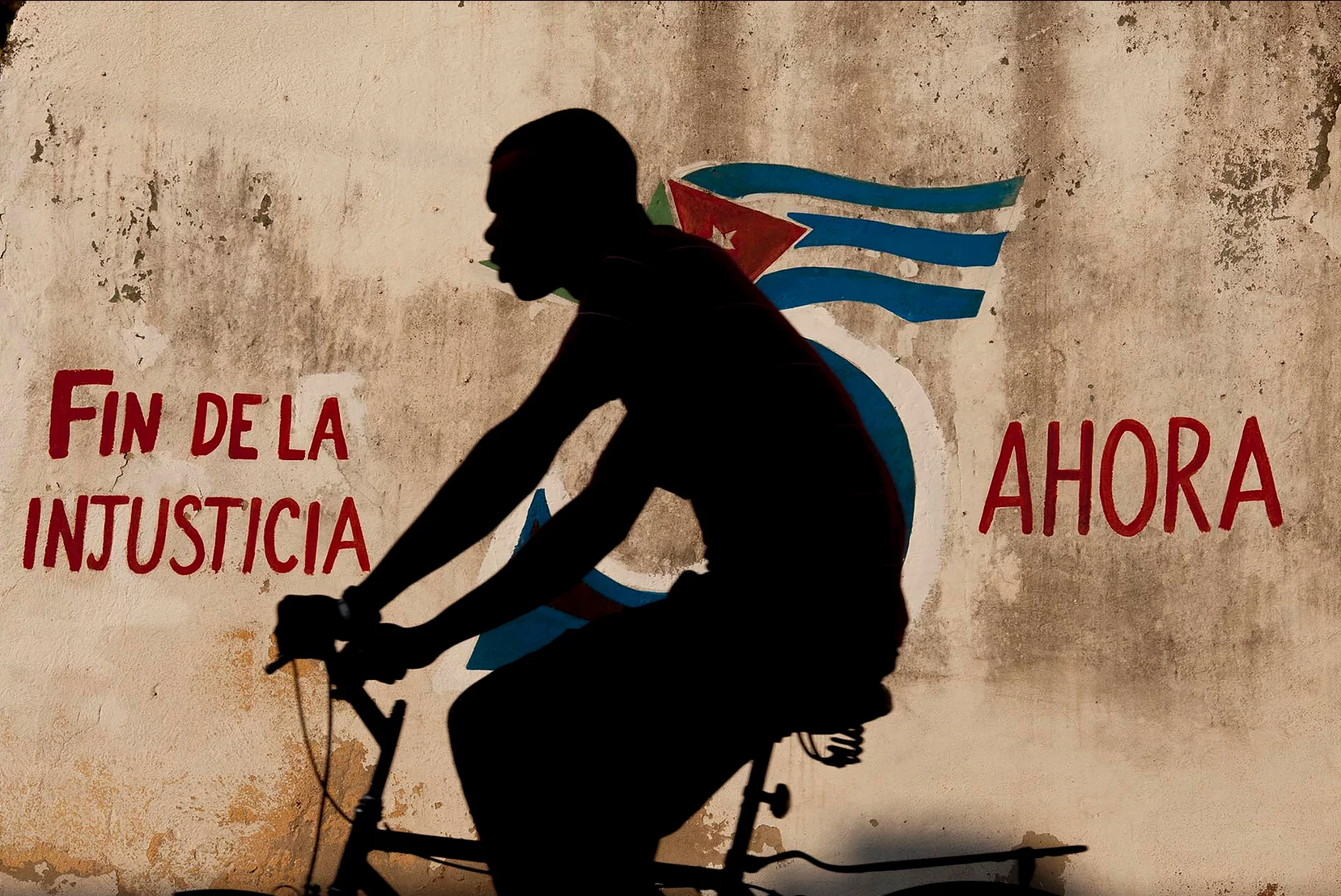 Color photo by Alex Almeida, boy cycling in front of cuban flag mural Cuba.