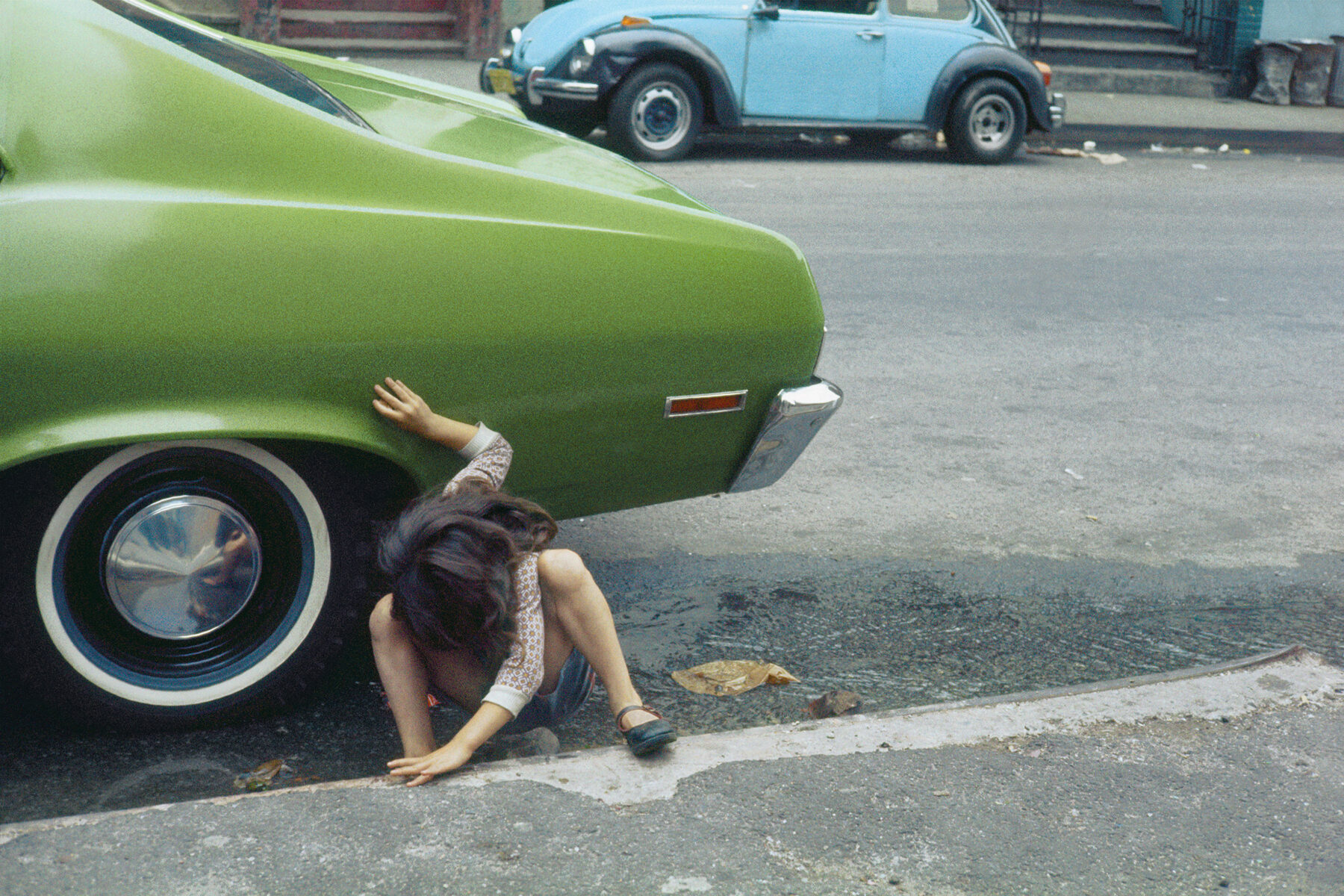 Color street photography by Helen Levitt, girl looking under green car, NYC