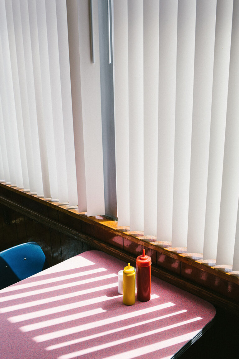 Color photo by Arnaud Montagard, mustard and ketchup on pink diner table. From the Road Not Taken