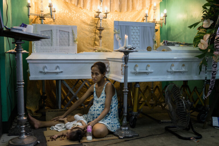 Elizabeth Navarro, 9 months pregnant, sits by the coffins of her partner, Domingo Manosca, and her son Francis, 6 years old on Wednesday, December 14, 2016 in Metro Manila, Philippines. Both were shot at home and are among the thousands who have died in President Rodrigo Duterte's bloody 'War on Drugs.' Documentary photography by Hannah Reyes Morales.