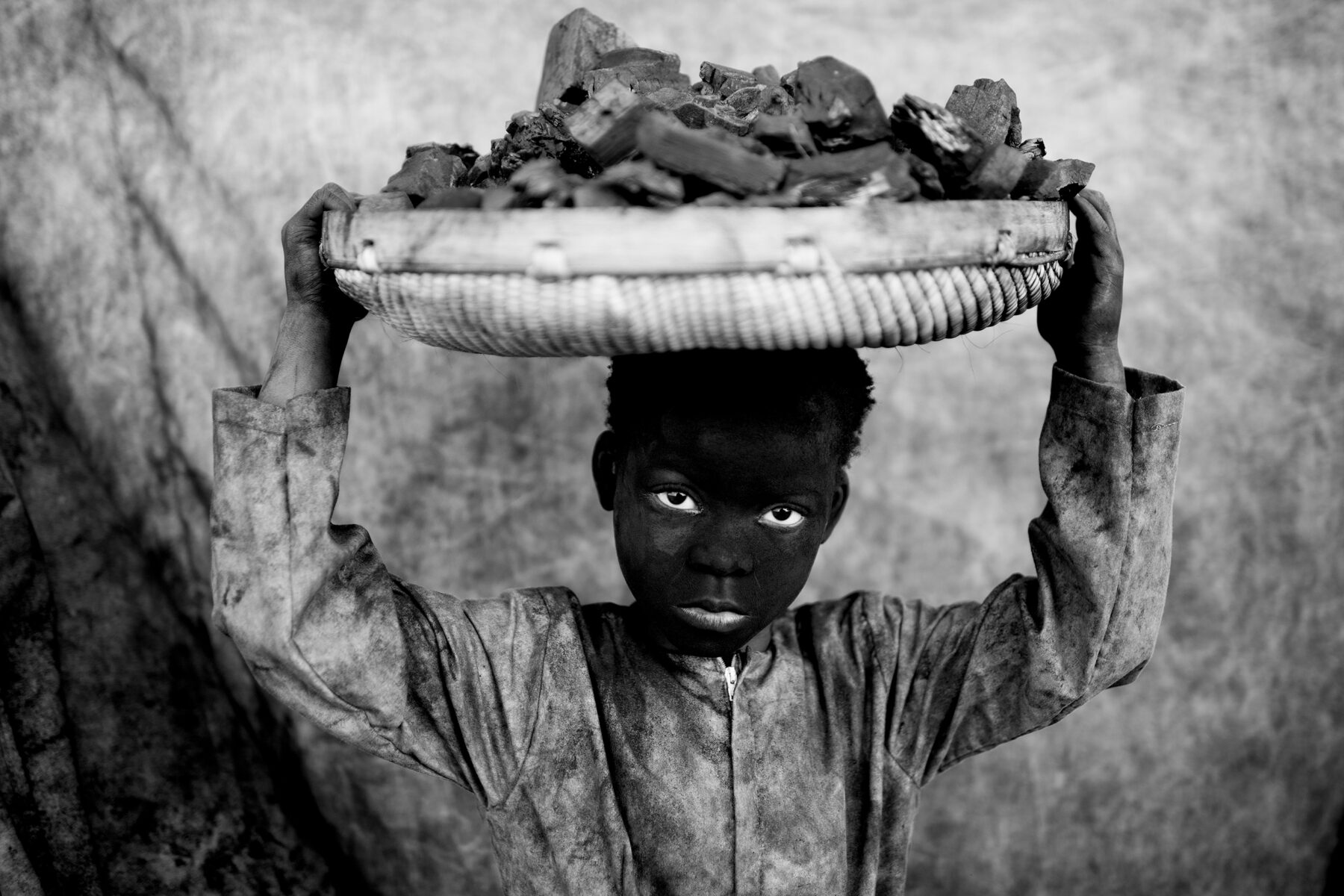 black and white photo of a kid carrying coal by Mário Macilau