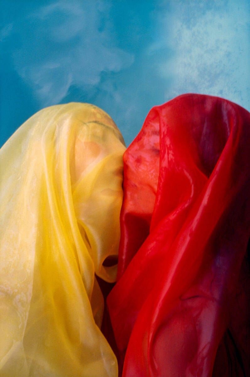 color photo of two people kissing under colorful cloth by Tyler Goldflower