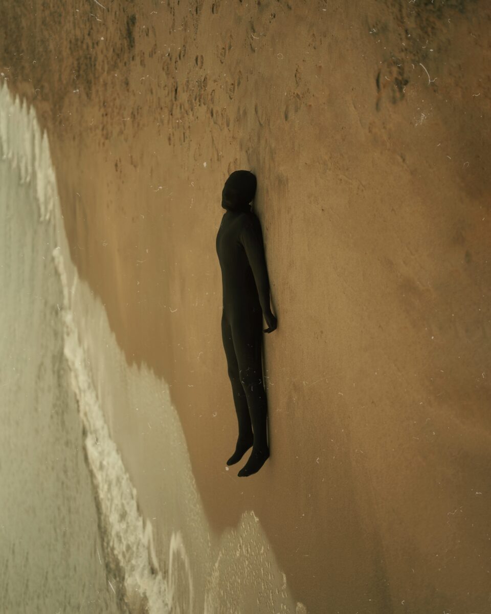 Color photography by Paolo Baretta. Portrait of figure in black outfit on beach