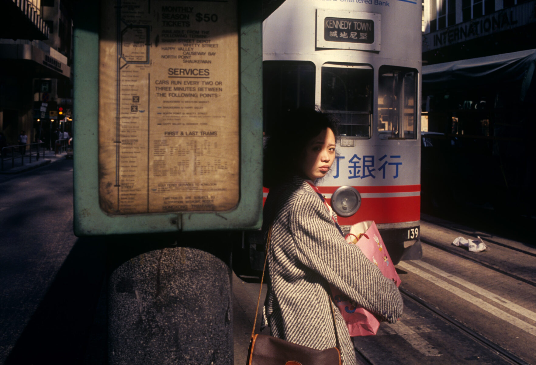 Color photography by Greg Girard, woman at tram stop, Hong Kong