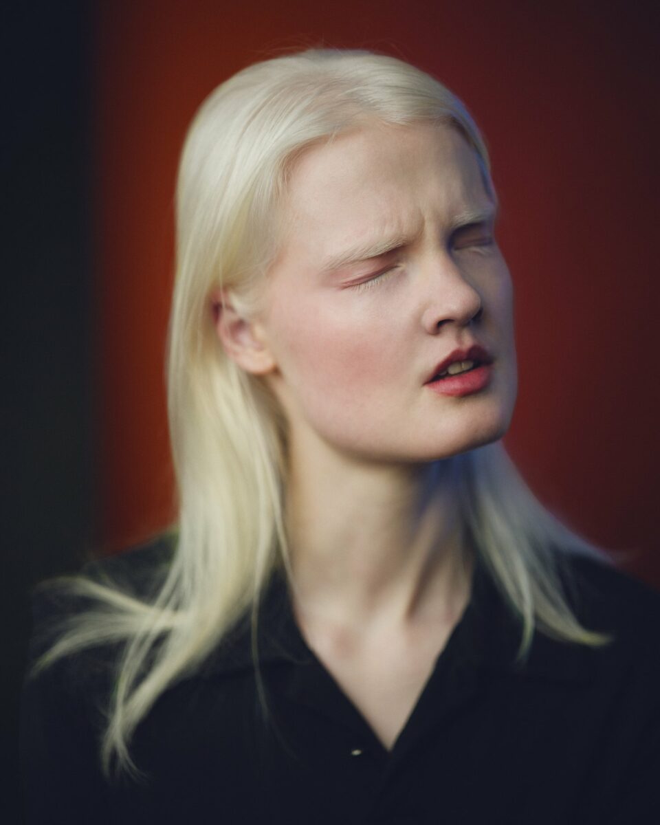 Portrait photography by Phil Sharp, woman with white/blonde hair and her eyes closed with red background