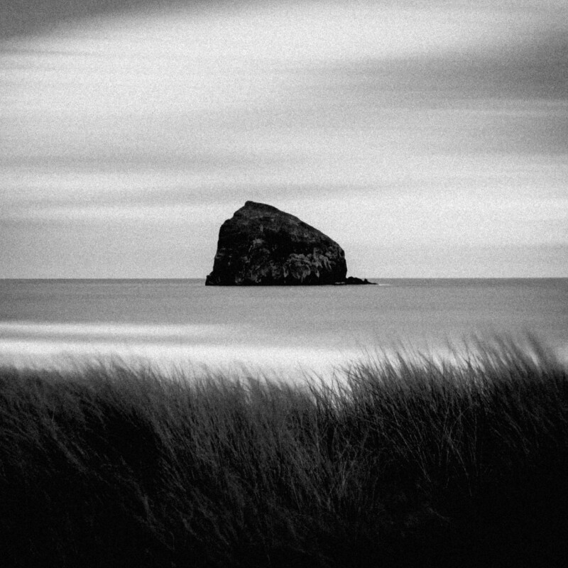 Black & white landscape photo by Adrian Vila. Black rocky island in the sea.