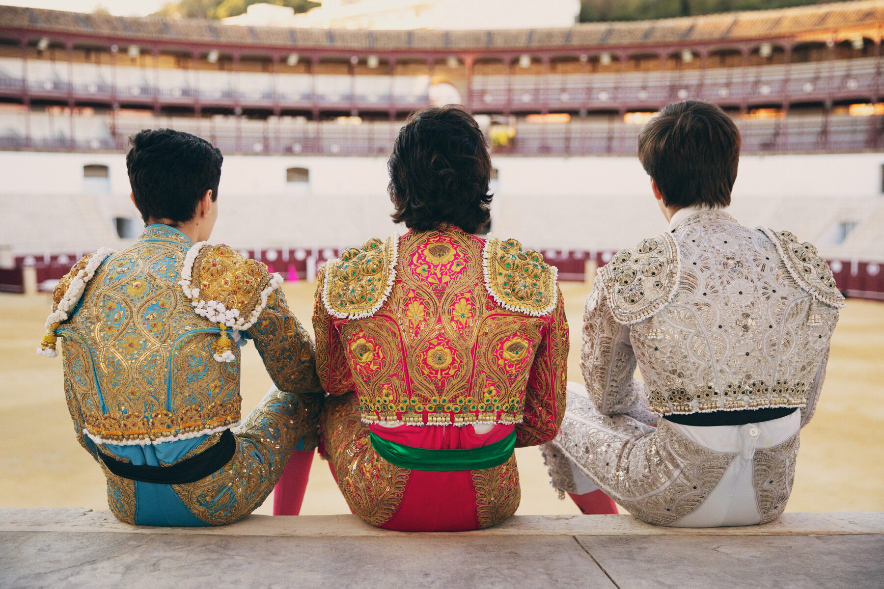 Portrait of a three young bullfighters from behind with a bullring in the background by photographer Owen Harvey