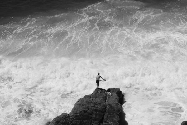 black and white landscape photo of coastline, waves and boy surfing by Matthew Bozec