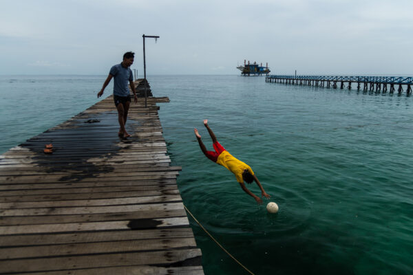 Color travel photography of two boys playing football on pier at Mabul island, Sabah, Malaysia by Emilio Fuliotti