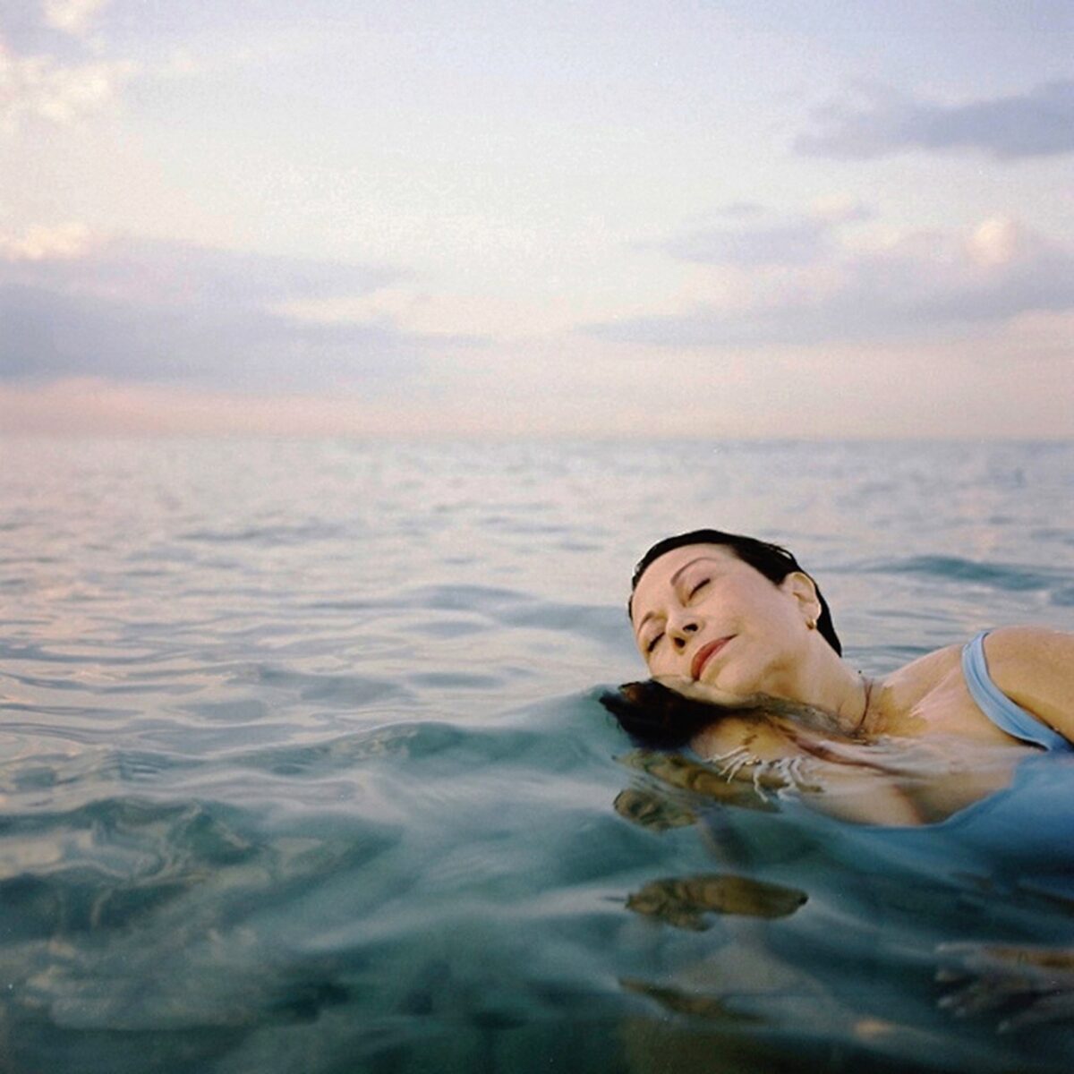 Photo of a woman with her eyes closed, swimming in the ocean