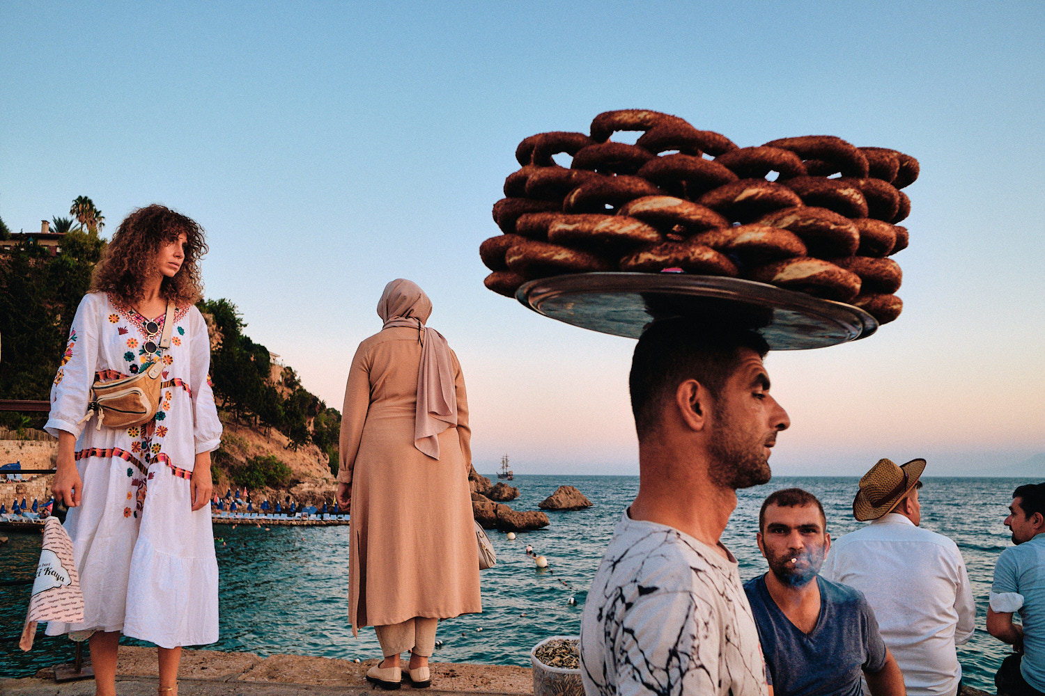 Street photography by Eduardo Ortiz. Man walking in front of the sea in Turkey with bread on his head