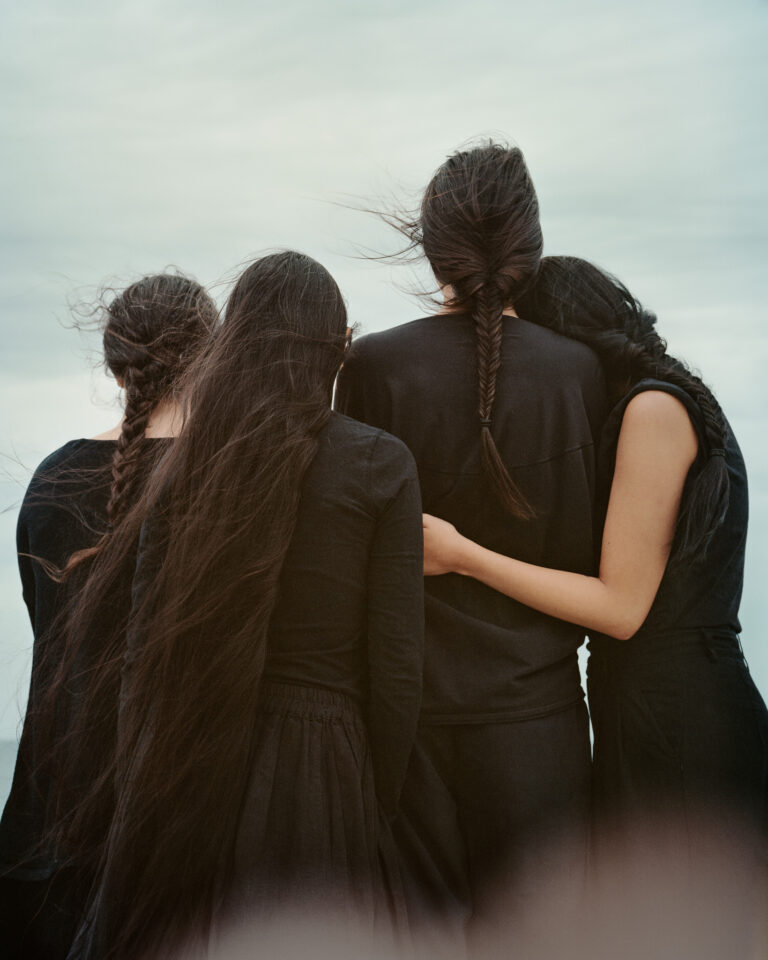 Photo of a group of women dressed in black embracing. Taken from behind