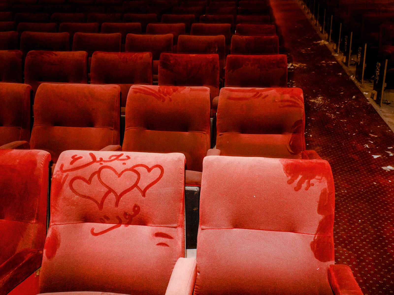 Photo of red cinema seats covered in dust with a heart and some arabic writing drawn on one