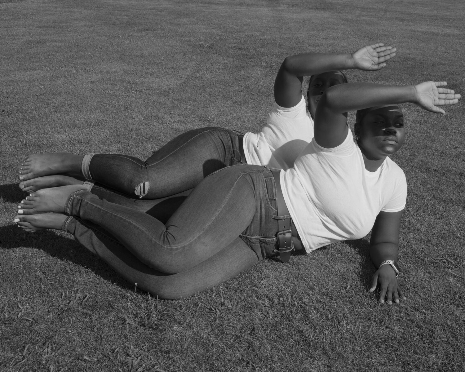 Black and white photo of two women dressed the same lying on the grass