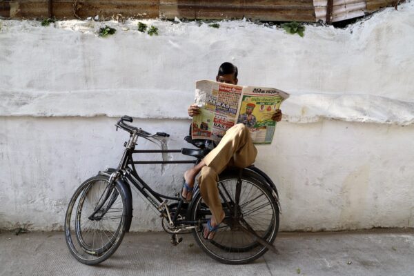 color street photo of man reading newspaper on bicycle in India by Raphael Eyraud