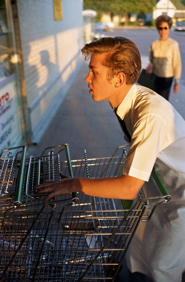 Color photography by William Eggleston. Boy pushing supermarket carts.