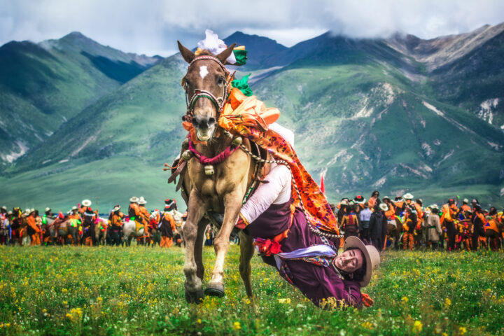 Color photo of an acrobatic horse rider with mountains in the backdrop in Tibet