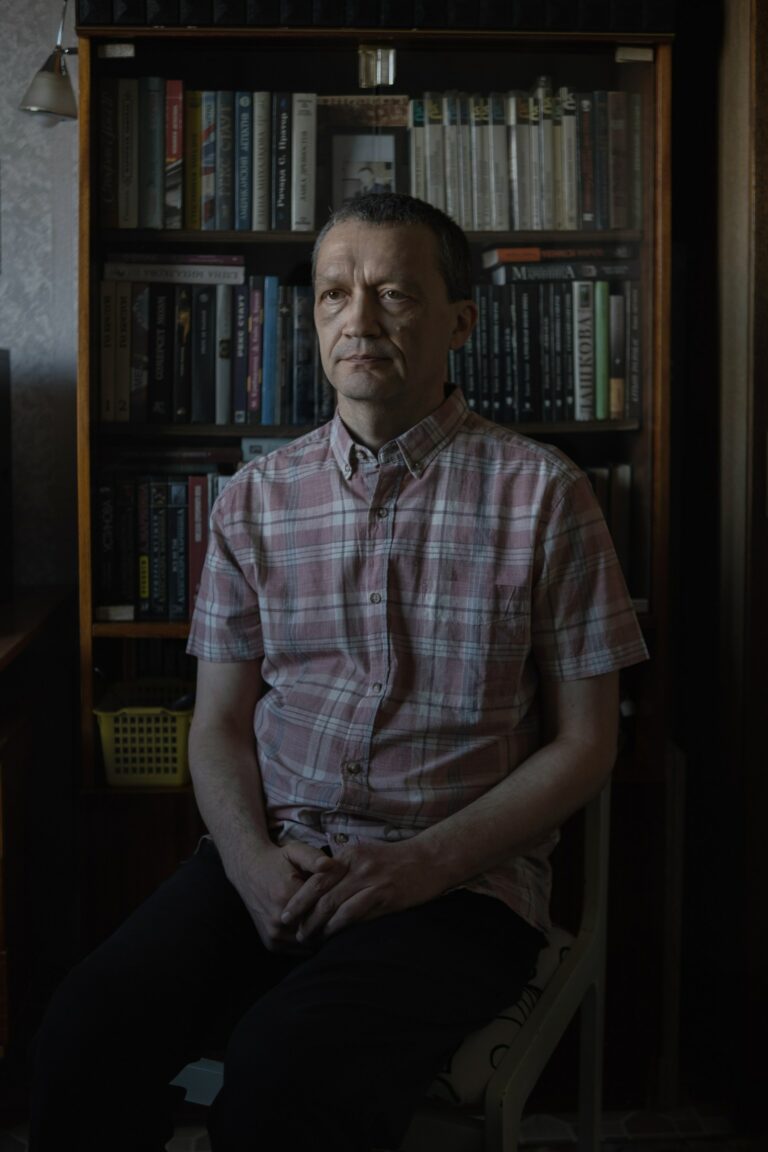 Portrait photography of a man in front of a bookcase by Kseniya Maksimova.