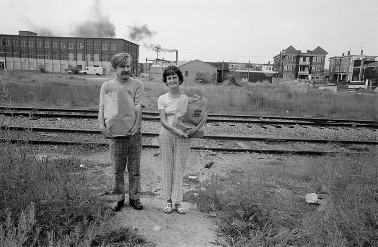 Black & white photography by Sage Sohier, portrait of a couple with factories in the background