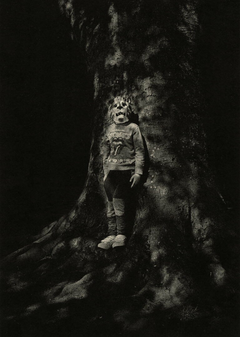 Black & white photography by Dominic Turner. Boy in mask stood against a tree