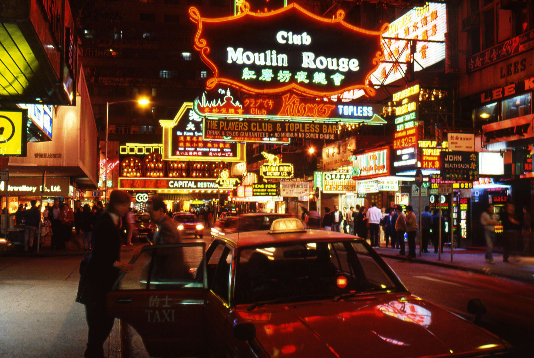 Photo of neon signs and taxis on the street in Hong Kong 1987, by Greg Girard